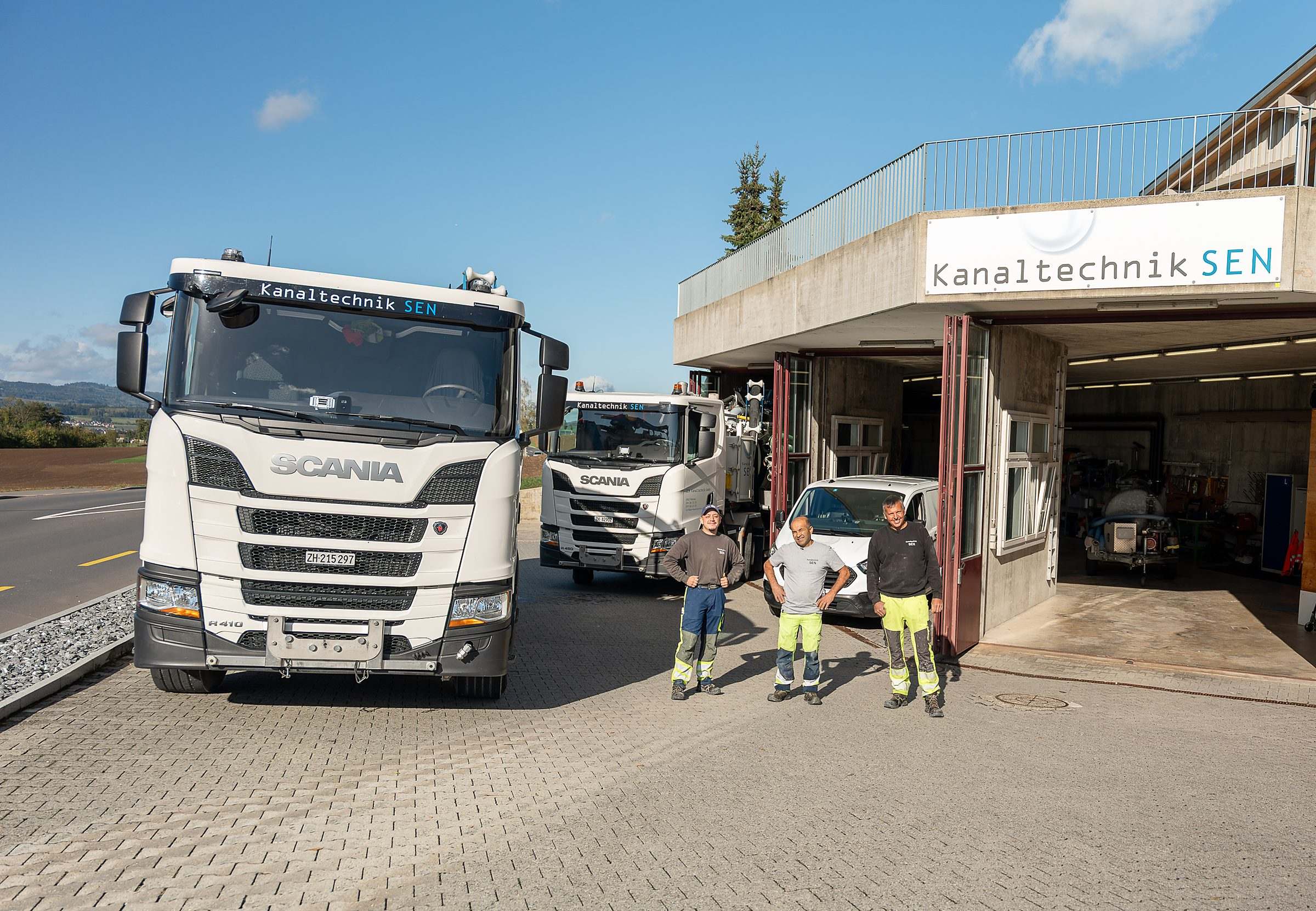 Firmengelände der SEN Kanaltechnik in Obfelden: zwei Saug- und Spülwagen, das Team und das Gebäude mit dem Firmenschild